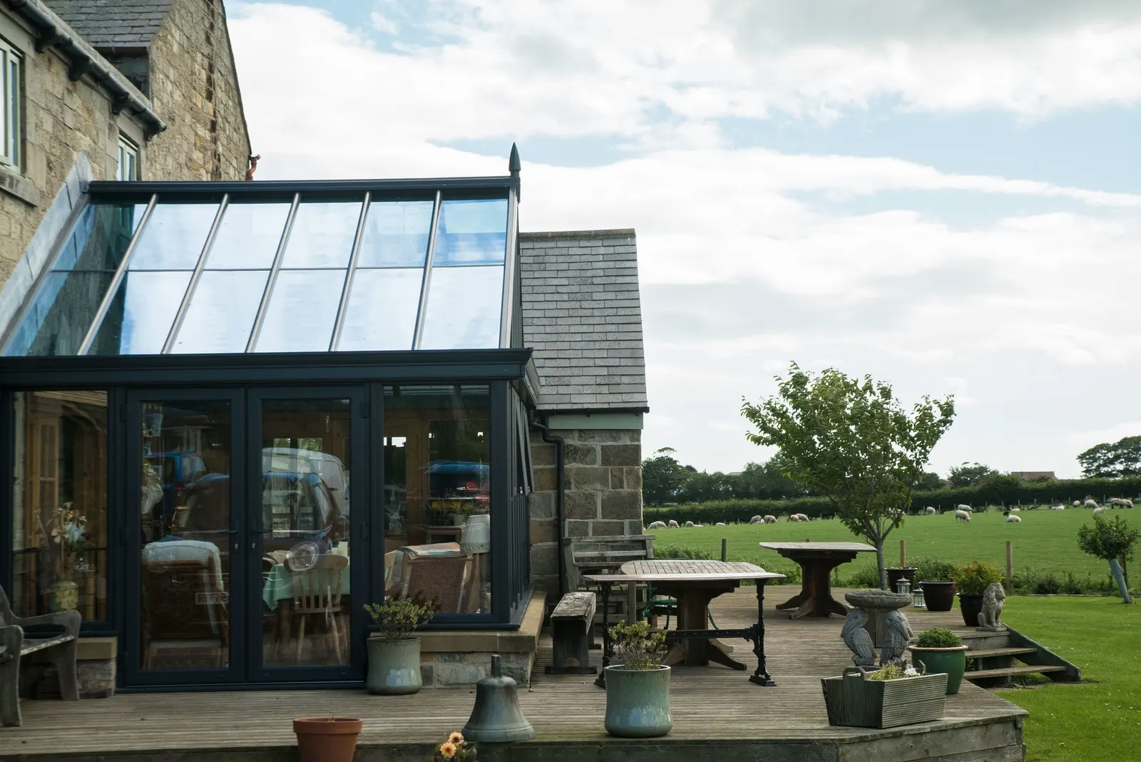 An anthracite-framed conservatory with a glazed roof, on the back of a stone house
